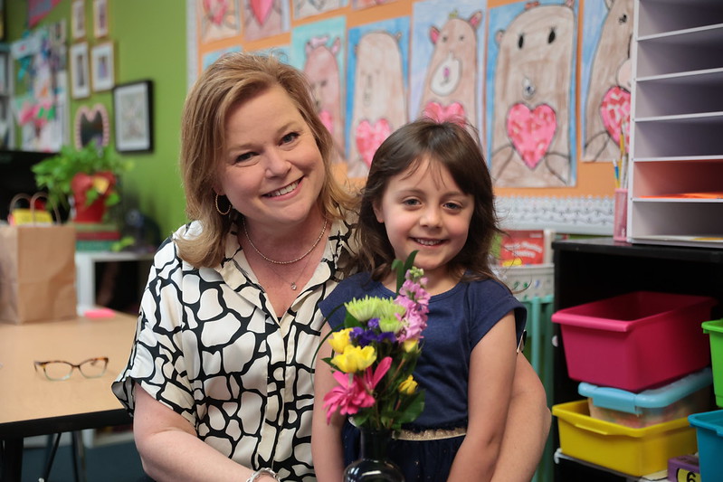 Two girls sitting and smiling in front of a climbing wall.